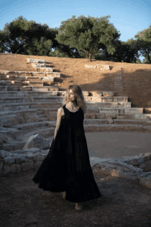 a woman in a long black dress stands in front of a stone amphitheater