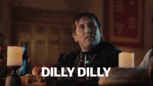 a man is sitting at a table with candles and the words `` dilly dilly '' written on the screen .