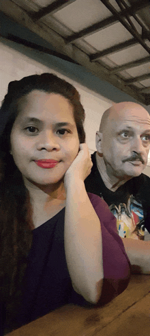 a bald man with a mustache sits next to a woman with red lipstick