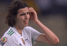 a soccer player with curly hair is scratching his head during a game .