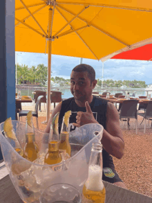 a man is sitting under an umbrella with a bucket of corona beer