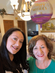 two women standing next to a balloon that says happy mothers day