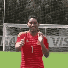 a man in a red soccer jersey is giving a thumbs up while standing in front of a soccer goal .