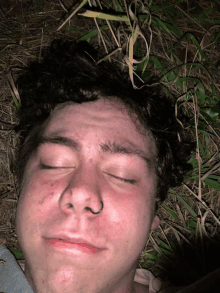 a man with a nose ring laying in the grass with his eyes closed