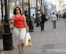 a woman in a red tank top is walking down a sidewalk carrying a bag that says ' tesco '