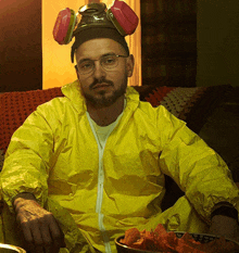 a man in a yellow coverall with a gas mask on his head sits on a couch