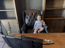 a little girl sits in a chair in front of a computer