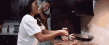 a man and a woman are preparing food in a kitchen with a carton of tomato juice on the counter