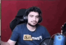 a man wearing headphones and a blue shirt that says pornhub is sitting in a chair .