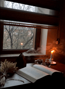 an open book sits on a table next to a cup of coffee and a lit candle