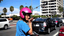 a woman wearing a pink helmet and a blue shirt has a license plate that starts with the letter i