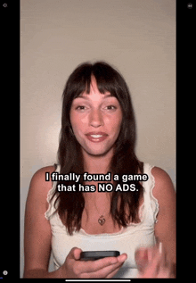 a woman in a white tank top is holding a cell phone and says i finally found a game that has no ads