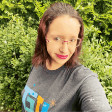 a woman wearing glasses and a t-shirt with the letter t on it takes a selfie