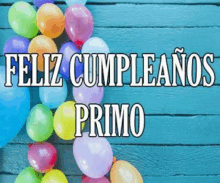 a bunch of colorful balloons on a blue wooden table with the words feliz cumpleanos primo in white letters