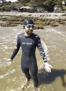 a man in a wetsuit is standing in the water on the beach .