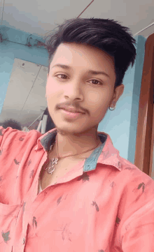 a young man wearing a red shirt and a necklace looks at the camera