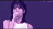 a woman is singing into a microphone while wearing a hat and a white tank top .