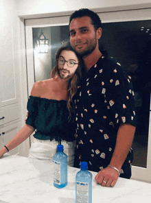 a man and a woman standing next to each other with a bottle of hot water on the countertop