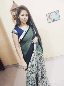 a woman in a green and white floral saree stands in front of a wall with a picture on it