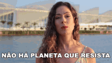 a woman stands in front of a body of water with the words " nao ha planeta que resista " below her