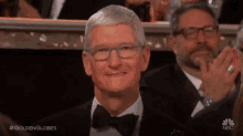 a man in a tuxedo and bow tie is smiling while sitting in the audience at a golden globes event .