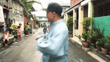 a man in a baseball cap is walking down a narrow street with a building with the letter b on it