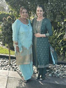 two women standing next to each other in front of trees