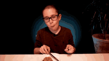 a young boy with glasses is sitting at a table with a plate of food and a knife and fork