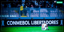 a soccer player sits on the field in front of a conmebol libertadores banner