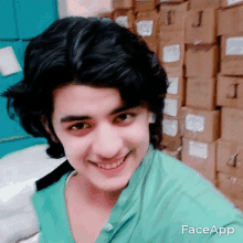 a young man in a green shirt smiles in front of a stack of cardboard boxes labeled j