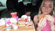 a woman sitting in a car eating a chicken sandwich from a box that says ' chicken ' on it