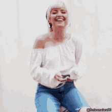 a woman wearing a white off the shoulder top is smiling