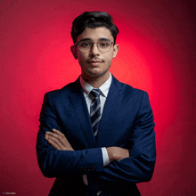 a man in a suit and tie stands with his arms crossed against a red background