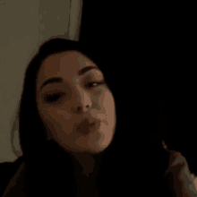 a woman is blowing a kiss in a dark room while looking at the camera .