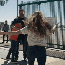 a woman is standing in front of a fence with her arms outstretched and a man is standing behind her .