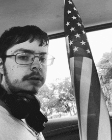 a man wearing glasses and headphones holds a small american flag