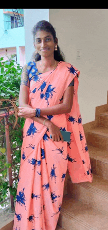 a woman in a pink floral saree is standing on a balcony holding a cell phone .