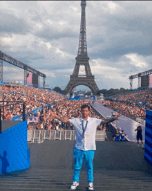 a man stands in front of the eiffel tower holding a medal