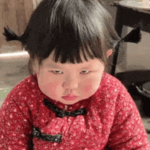 a little girl with pigtails and a red floral dress is making a funny face