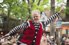 a man in a red and black striped shirt stands in front of a crowd with his arms in the air