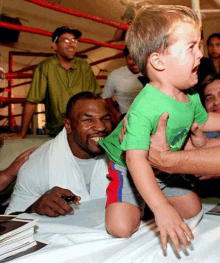 a young boy in a green shirt is being held by a man