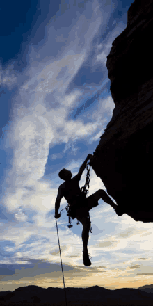 a silhouette of a man climbing up a cliff