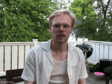 a man wearing glasses and a striped shirt is sitting on a porch with a white fence in the background