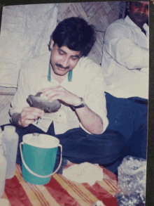 a man with a mustache is sitting on the floor with a green bucket on the table