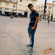 a young man in a striped shirt and jeans is standing on a sidewalk in a city square .