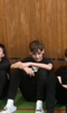 three boys are sitting on the floor in front of a wooden wall .