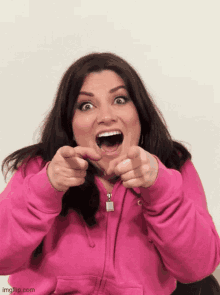 a woman in a pink hoodie points at the camera