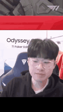 a man wearing glasses is sitting in a chair in front of an odyssey logo .