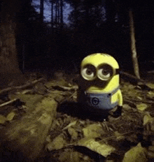 a toy minion is sitting on the ground in a dark forest .