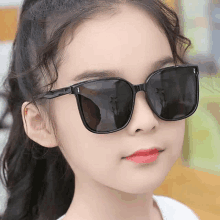 a young girl wearing a pair of black sunglasses looks at the camera